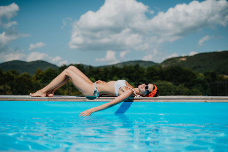 Young woman lying by the on edge of pool and sunbathing.