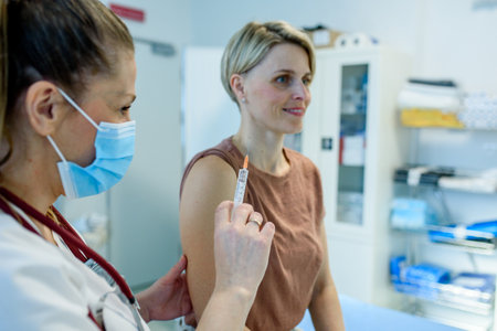 Doctor administering vaccine to womans arm during routine immunizationの写真素材