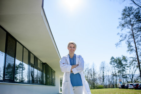 Young female doctor taking a break, standing in front of hospital.の写真素材