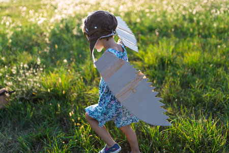 Little girl playing on a meadow in nature, with goggles and wings as if flying.の写真素材