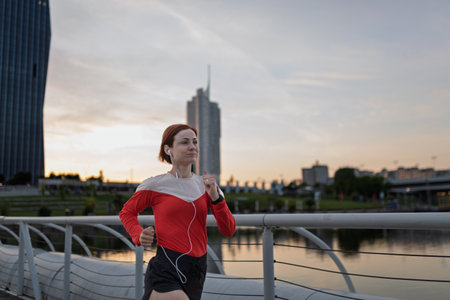 sporty woman running across a city bridge during her morning workout.