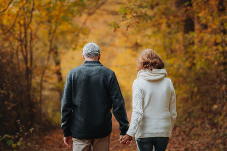 Elderly couple walking hand in hand through autumn forestの写真素材