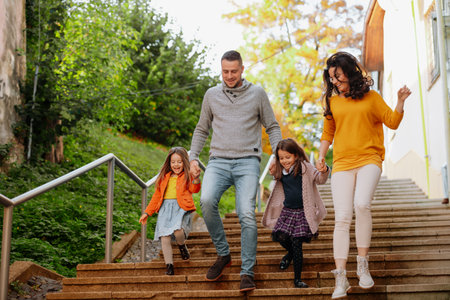 Sisters and parents jumping down the stairs in park during warm autumn day.