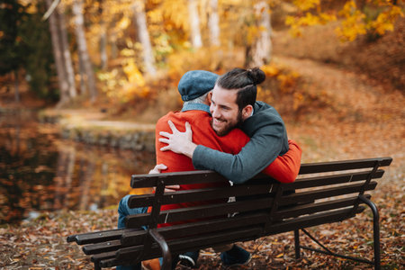 Grandad and grandson sitting on bench in park and hugging.