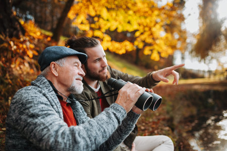 Senior father and his son with binoculars in nature, talking.