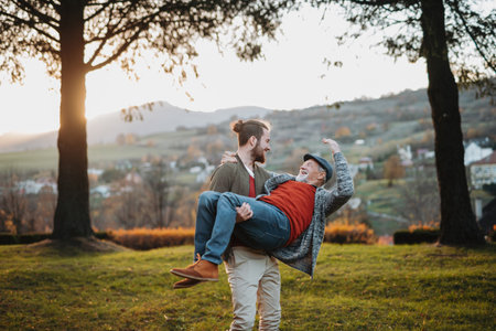 Adult son holding his father in arms, having fun in autumn nature.の写真素材