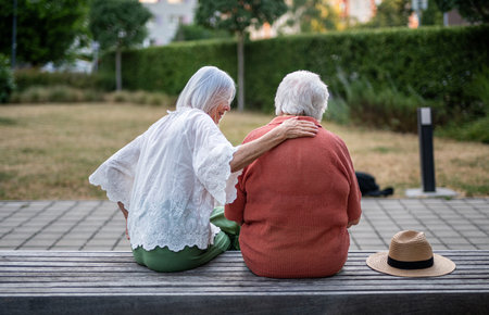 Elderly mother sitting on bench with adult daughter.の写真素材