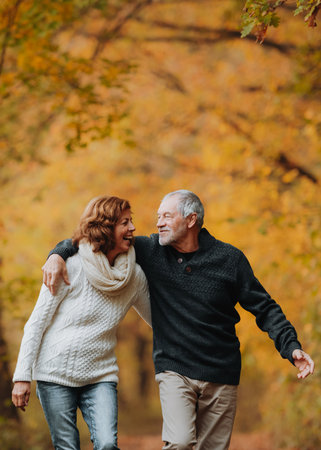 Romantic walk through fall forest by senior couple.