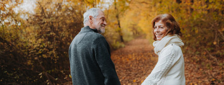 Retired couple standing in the middle of colorful autumn woods.の写真素材