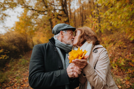 Senior man and woman enjoying a walk in fall, holding fallen leaves.の写真素材