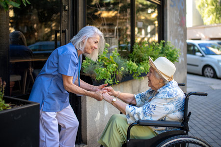 Tender moment between older caregiver and senior female patient in wheelchair.