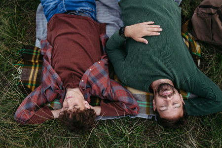 Top view of father and teen boy lying in grass and resting during hiking trip.
