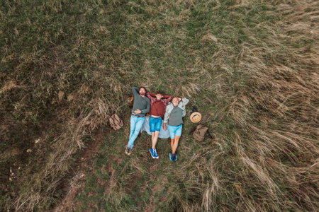 Areal view of grandfather, father and teen boy lying in grass and resting during hiking trip.