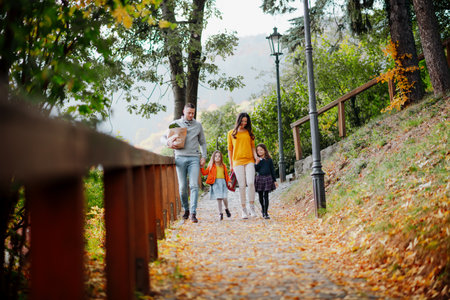 Sisters and parents walking in park during warm autumn day.の写真素材