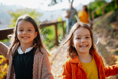 Sisters with parents in the background walking in park during warm autumn day.の写真素材