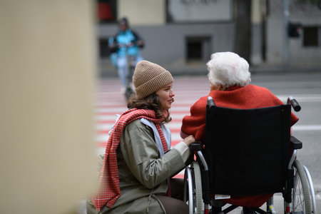 Granddaughter on an autumn walk in the city with her grandmother, pushing her in wheelchair. Rear view.の写真素材