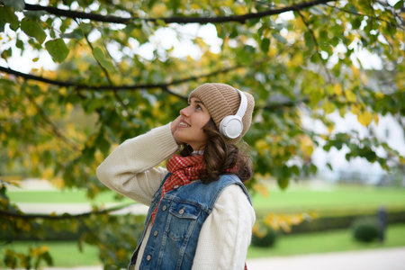 Beautiful young woman on a walk in the autumn park, listening to music and enjoying a peaceful...