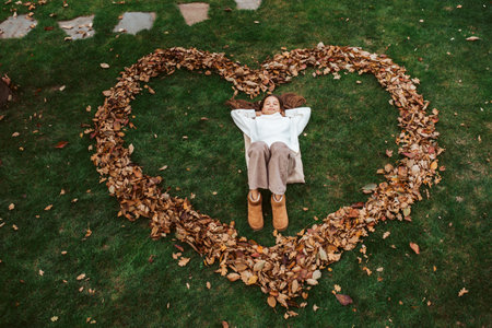 Portrait of teen girl laying on grass in the middle of heart from leaves.