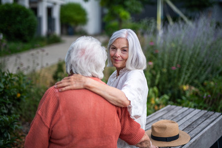 Elderly mother sitting on bench with adult daughter.の写真素材