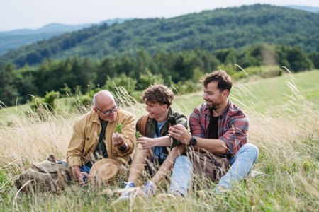 Grandfather, father and teen boy hiking togeter in nature, resting on meadow.の写真素材