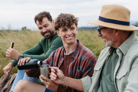 Grandfather, father and teen boy hiking togeter in nature, having cup of tea.の写真素材