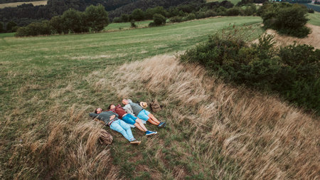 Areal view of grandfather, father and teen boy lying in grass and resting during hiking trip.