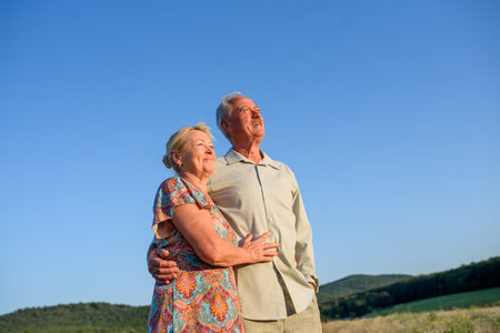 Happy senior couple embracing in meadow at sunset.の写真素材