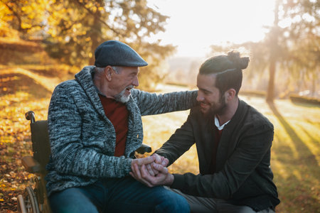 Grandson pushing his older grandad in wheelchair during walk in fall nature.の写真素材