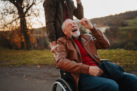 Grandson joking with his older grandad in wheelchair during walk in fall nature.の写真素材
