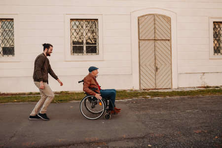 Grandson joking with his older grandad in wheelchair during walk in fall nature.の写真素材
