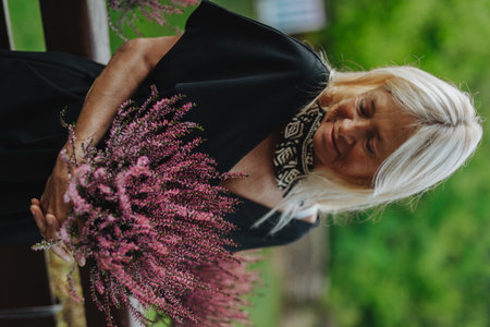 Mature woman standing by potted heathers on terrace.の写真素材