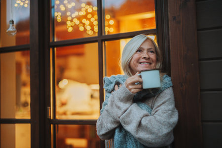 Senior woman enjoying warm tea on terrace during cold autumn evening.の写真素材