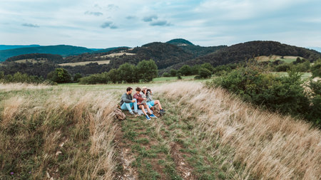 Grandfather, father and teen boy sitting in grass and resting during hiking trip.