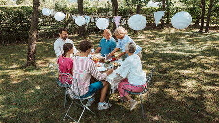 Aerial shot of family gathering for barbecue in summer garden, talking and eating grilled food.