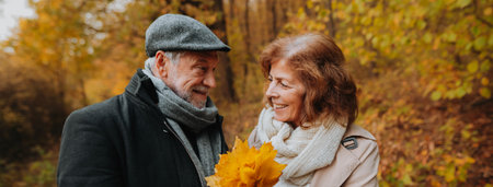 Senior man and woman enjoying a walk in fall, picking fallen leaves.