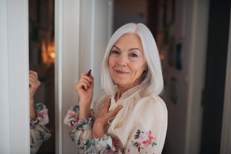 Senior woman applying makeup in front of mirror.