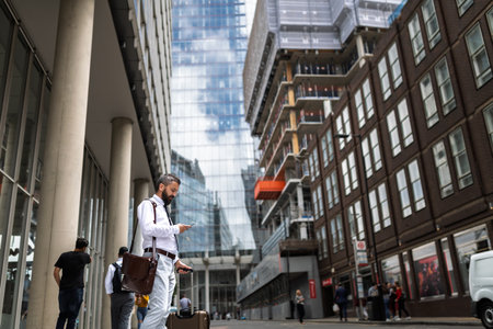 Man with suitcase walking down the street, looking at phone.の写真素材