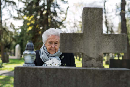 Elderly widow bringing flowers to a grave at cemetery.