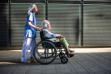 Older nurse pushing senior woman in wheelchair and talking with her.