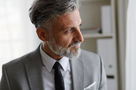 Portrait of mature businessman standing in an office, holding a tie.