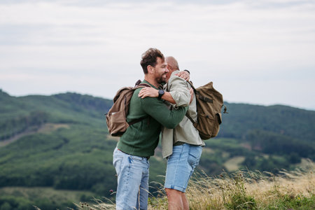 Adult son and older father hiking togeter in nature, hugging after finishing track.