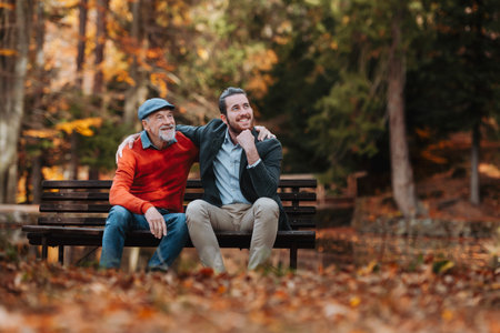 Son and older father sitting on bench by lake and talking.の写真素材