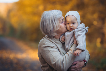 Grandmother kissing baby outdoors in autumn nature.の写真素材