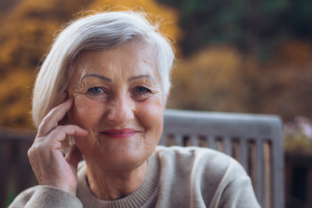 Portrait of smiling elderly lady relaxing on terrace during warm autumn day.の写真素材