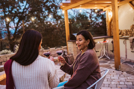 Elderly mother and adult daughter having glass of wine together, sitting by fire pit.の写真素材