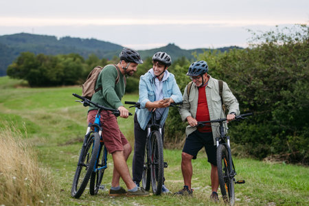 Grandfather, father and teen boy on cycling trip looking at map in smartphone.の写真素材