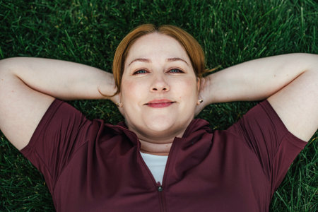 Beautiful plus size woman lying on grass after outdoors training session.の写真素材