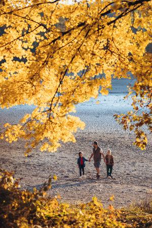 Father holding hands with his two kids during fall walk.