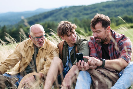 Grandfather, father and teen boy hiking togeter in nature, resting on meadow.の写真素材