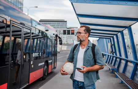 Handsome man boarding bus, holding sport ball and phone.の写真素材